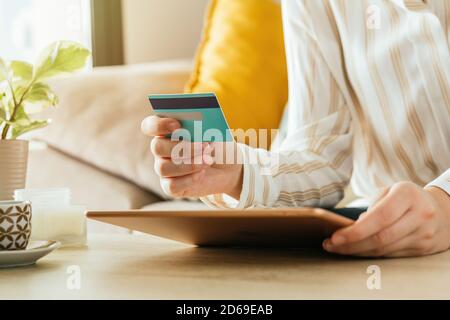 Photo d'une femme caucasienne méconnaissable faisant des achats en ligne avec la tablette et une carte de crédit du canapé dans le salon. Concept de commerce électronique Banque D'Images