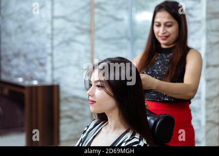 Une coiffeuse de cheveux fournit des services de coiffage à une femme indienne jolie jeune, belle femme obtient ses cheveux fait à un salon, foyer sélectif. Banque D'Images