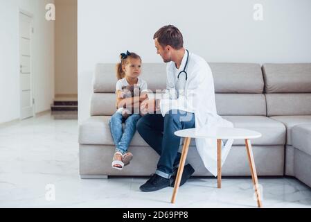 Le médecin masculin en uniforme blanc est assis dans la clinique avec petite fille Banque D'Images