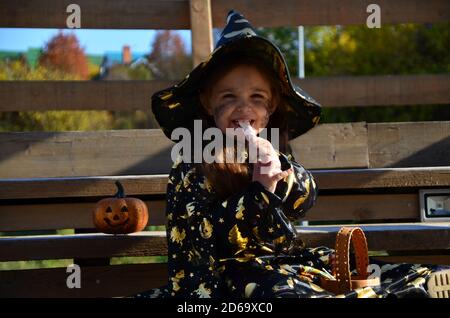 Une fille dans un costume de sorcière et un chapeau noir sur la tête avec le maquillage noir d'Halloween, zombie mangeant sucreries jelly Worms à une célébration d'Halloween Banque D'Images