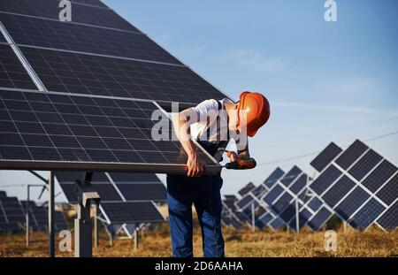 À l'aide d'un tournevis sans fil. Homme travaillant en uniforme bleu à l'extérieur avec des piles solaires à la journée ensoleillée Banque D'Images