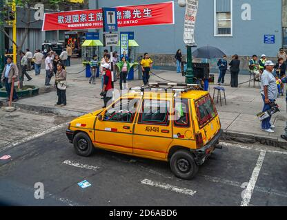 Lima, Pérou - 4 décembre 2008 : la bannière rouge accueille le président chinois Hu Jintao dans une rue commerciale avec des piétons et une voiture jaune. Banque D'Images