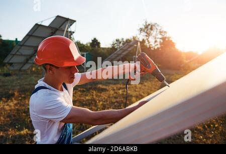 À l'aide d'un tournevis sans fil. Homme travaillant en uniforme bleu à l'extérieur avec des piles solaires à la journée ensoleillée Banque D'Images