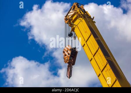 Flèche jaune d'une grue de chargement contre un ciel bleu avec des nuages. Banque D'Images