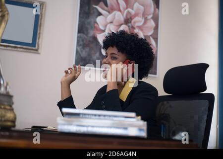 Photo sous angle d'une femme afro-américaine assise sur un chaise derrière un bureau dans un bureau Banque D'Images