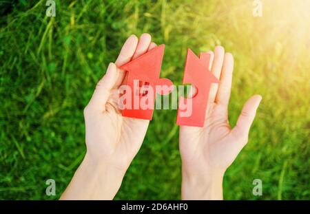 Maison rouge avec une forme de deux parties de puzzle dans les mains humaines. Banque D'Images