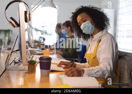 Femme portant un masque facial prenant des notes au bureau Banque D'Images