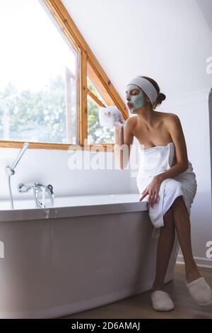 Femme avec masque soufflant de la mousse tout en étant assis sur le bord de baignoire Banque D'Images