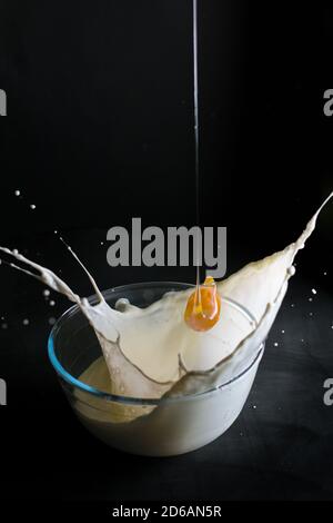 Œuf tombant dans un bol avec du lait et barbotant sur fond noir. Banque D'Images