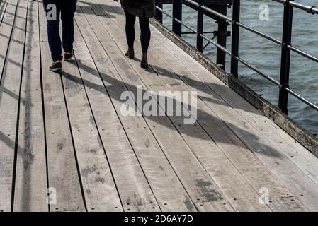 Couple, deux personnes, marchant sur Southend Pier, Southend on Sea, Essex, Royaume-Uni. De longues ombres sur une passerelle en bois. Ombre. Jambes uniquement Banque D'Images