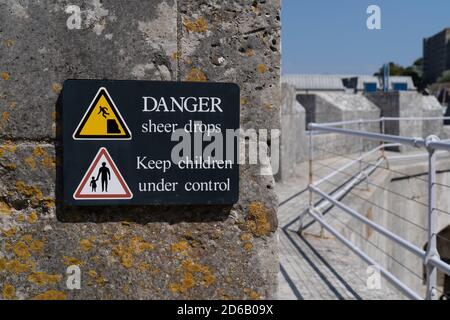 Danger de chute soudaine triangle d'avertissement jaune avec symbole de homme tombant d'un bord de falaise et garder les enfants sous signe de contrôle sur rampage Banque D'Images