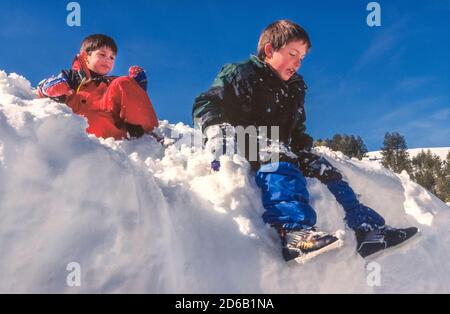 Deux jeunes garçons américains en vacances se sont amusés à glisser sur un remblai de neige lors d'une journée d'hiver ensoleillée dans les montagnes Sawtooth de l'Idaho, aux États-Unis. En hiver, le Sawtooth National Recreation Area est un vaste terrain de jeux enneigé avec des kilomètres de pistes pour le ski de fond, la raquette et la motoneige. Banque D'Images