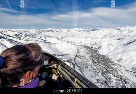 Une touriste féminine à bord d'un vol touristique d'hiver en planeur regarde à travers la canopée claire du voilier dans les Smoky Mountains enneigées et la Wood River Valley qui abrite les villes voisines de station balnéaire, Ketchum et Sun Valley, deux destinations de vacances populaires dans l'Idaho, aux États-Unis. La région pittoresque compte de nombreux pistes de ski de débutant à expert qui attirent les skieurs et les snowboarders tout au long de la saison d'hiver. Banque D'Images