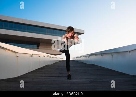 Jeune sportif exécutant des mouvements articulaires de yoga dans une zone urbaine de la ville. Banque D'Images