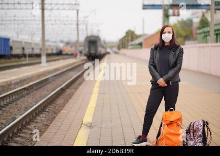 Femme dans un masque de protection en attente de train sur la plate-forme. Pleine longueur de passager féminin dans un masque de protection avec sacs à dos debout sur le chemin de fer Banque D'Images