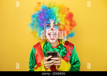 Clown se tenant sur fond jaune insolé, souriant et bavardant avec son téléphone Banque D'Images