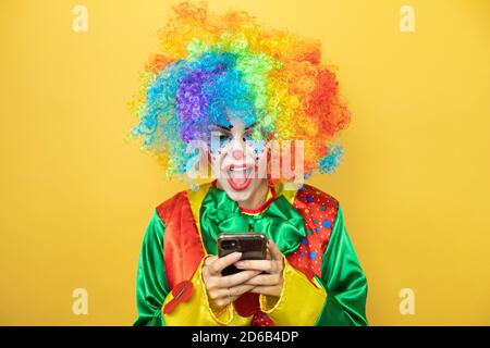 Clown se tenant sur fond jaune insolé, souriant et bavardant avec son téléphone Banque D'Images