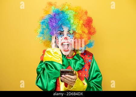 Clown se tenant sur fond jaune insolé jaune discutant avec elle téléphone et surpris Banque D'Images