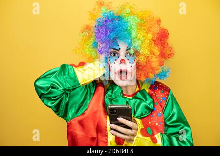 Clown se tenant sur fond jaune insolé jaune discutant avec elle téléphone et surpris Banque D'Images