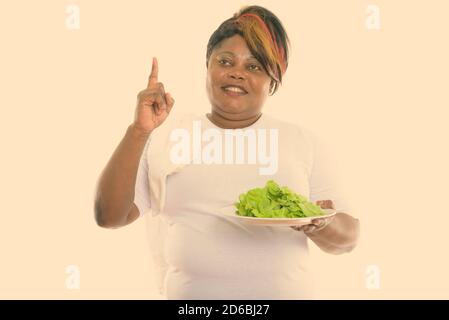 Femme africaine noire grasse mûrie attentionnés souriant tout en tenant la laitue servi sur une assiette blanche et pointant vers le haut Banque D'Images