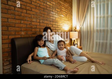 petite sœur joyeuse souriante et assise avec sa mère sur le lit dans la nuit Banque D'Images