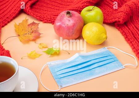 Feuilles d'érable, grenade, citron, pomme, tasse de thé, masque médical, foulard rouge, maquette sur fond orange. Concept, automne, vitamines pour la santé, quarantaine due au coronavirus. Photo de haute qualité Banque D'Images