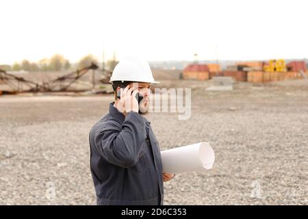 Contremaître caucasien parlant par le talkie-walkie VHF et des documents sur le chantier de construction. Banque D'Images