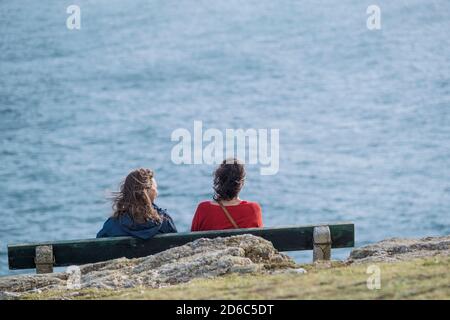 Deux amies assises sur un banc surplombant la mer sur la côte de Newquay, dans les Cornouailles. Banque D'Images