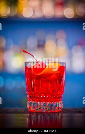Negroni. Cocktail de boisson rouge dans un pot en verre avec zeste de cerise et d'orange et effet bokeh. Banque D'Images