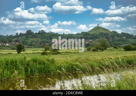 Glastonbury Tor au loin sur une journée ensoleillée et lumineuse. Somerset, Angleterre. Tor à droite de l'image avec un ruisseau local et des terres agricoles en premier plan. Banque D'Images