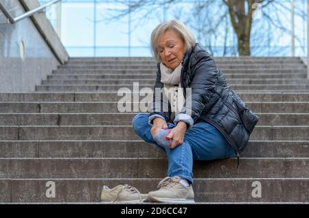 Senior femme sans défense en massant son pied à revivre et courbatures après tomber comme suit Banque D'Images