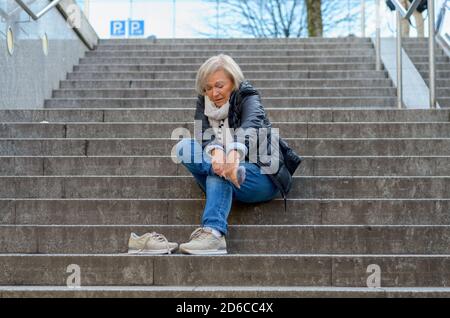 Senior femme sans défense en massant son pied à revivre et courbatures après tomber comme suit Banque D'Images