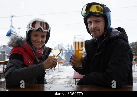 Femme et homme, mari et femme, buvant de la bière et du vin dans un restaurant sur une piste de ski pendant une pause de ski dans l'après-midi, par une journée nuageuse Banque D'Images