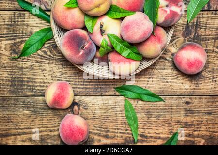 Pêches fraîches mûres dans un panier sur une table rustique en bois, vue sur le dessus. Fruits biologiques sains. Banque D'Images