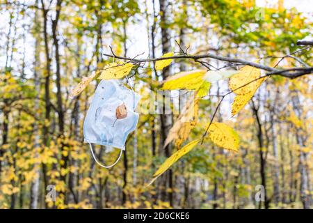 masque médical sale accroché à la branche de l'arbre avec du jaune laisse dans le parc de la ville le jour de l'automne Banque D'Images