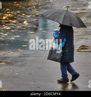 Une personne avec un parasol traverse la pluie. Une personne avec un parasol marche dans une rue humide. Personne avec parapluie sous la pluie. L'automne part sur le WE Banque D'Images