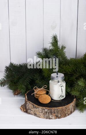 Bougie dans un pot en verre et biscuits sur une bûche en bois près d'une branche d'épinette sur un fond blanc. Banque D'Images