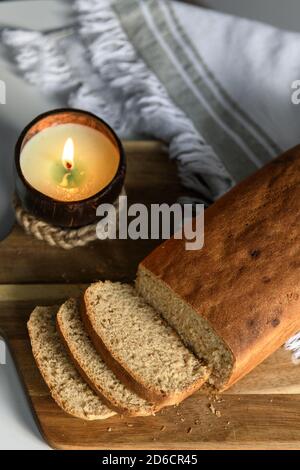 Tranché du pain fait maison sur une planche à découper en bois avec un bougie sur une serviette blanche Banque D'Images