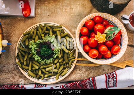 Vue de dessus des tomates rouges et des petits cornichons dans des assiettes vintage sur une table avec toile de jute. Banque D'Images