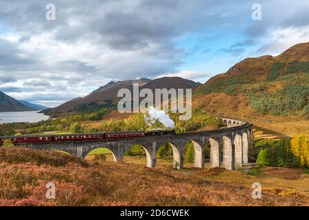 FORT WILLIAM SCOTLAND LE TRAIN À VAPEUR JACOBITE TRAVERSANT LE GLENFINNAN VIADUC AUX COULEURS DE L'AUTOMNE DANS LE PAYSAGE ET LE LOCH SHIEL DANS LA DISTANCE Banque D'Images