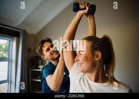 Physiothérapeute masculin corrigeant l'alignement du bras de la patiente tenant des poids assis dans le studio de pilates. Banque D'Images