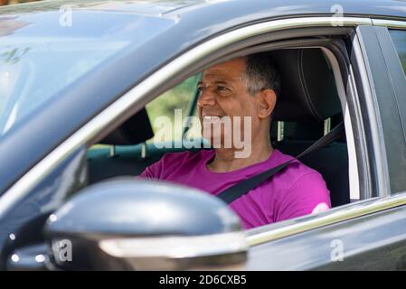 Homme âgé conduisant une voiture. Un homme à la retraite senior de la peau sombre du Moyen-Orient conduisant une voiture, portrait du côté. Banque D'Images