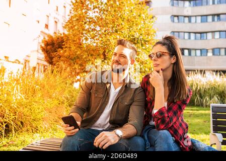 Un couple assis sur un banc de parc dans la ville essayant d'obtenir l'orientation avec l'aide du smartphone. Banque D'Images