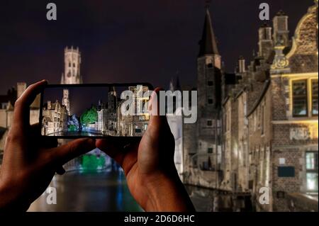 Touriste prenant des photos de la vieille ville de Bruges avec ses bâtiments et ses canaux historiques et la tour du Beffroi la nuit, Bruges, Belgique Banque D'Images
