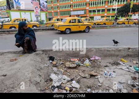 21.02.2011, Kolkata, Bengale-Occidental, Inde - UN homme sans-abri se squat sur le côté de la route à la recherche de restes utilisables pendant qu'un corbeau le regarde enviouss Banque D'Images