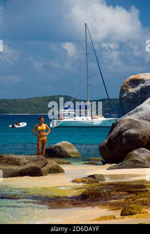 Jeune femme en maillot de bain jaune barboter aux bains, Virgin Gorda, grands rochers sur la plage, bateau à voile ancré en arrière-plan Banque D'Images