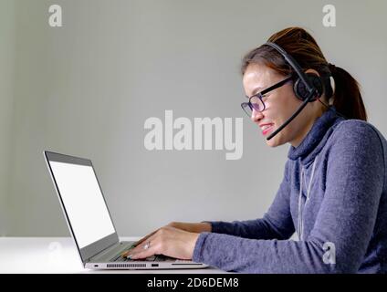Un jeune opérateur téléphonique de soutien souriant dans un casque avec ordinateur portable, sur fond gris avec ordinateur portable sur écran blanc Banque D'Images