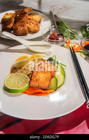 Soupe thaïlandaise de nouilles de riz au curry rouge accompagnée de tofu frits croustillants et d'œufs durs Banque D'Images