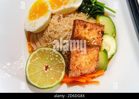 Soupe thaïlandaise de nouilles de riz au curry rouge accompagnée de tofu frits croustillants et d'œufs durs Banque D'Images