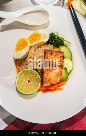 Soupe thaïlandaise de nouilles de riz au curry rouge accompagnée de tofu frits croustillants et d'œufs durs Banque D'Images